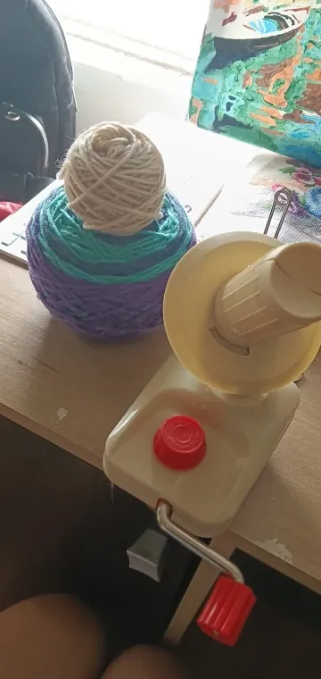 Ball winder clamped to a table next to two finished balls of yarn, photo from a verified buyer